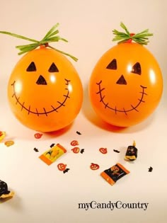 two orange balloons with faces drawn on them sitting next to candy candies and confetti