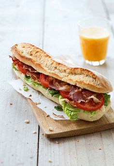 a sandwich with meat, lettuce and tomato on a cutting board next to a glass of orange juice