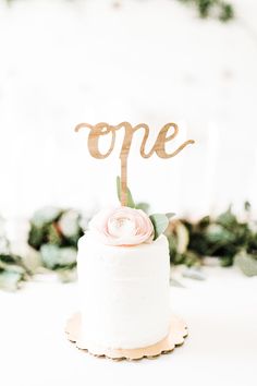 a white cake topped with a pink flower and the word'one'on top