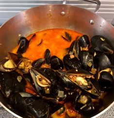 a pan filled with mussels and sauce on top of a stove burner