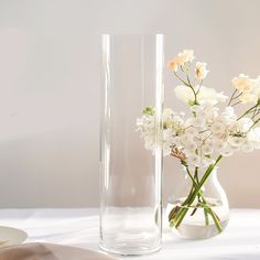 white flowers are in a clear vase next to a plate on a table with napkins