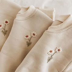 three sweaters with daisies embroidered on them