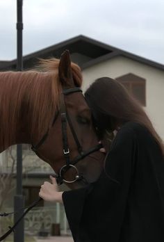 a woman is kissing the nose of a brown horse in front of a white building