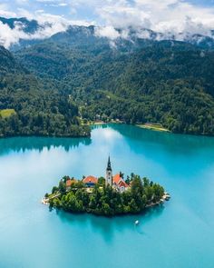 an island in the middle of a lake surrounded by trees and mountains with a church on it