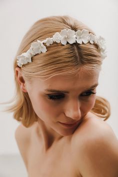 a woman wearing a headband with white flowers on it's head and her hair pulled back