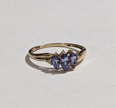 10k Solid Gold Tanzanite Ring with Beautiful Purple Diamond Accents. This ring approximately weighs 1.15 GRAMS and is marked and tested 10K YELLOW GOLD. 3 center stones are marquise-cut Tanzanite.  Central stone 6x3 0.25 Carat Weight 2 Side Stones 5x3 0.2 Carat Weight Total 0.65 Carat Weight Signed STS (Hallmark for designer Chuck Clemency) Size: 6.75 The top Of the Ring Measures Approximately: 7mm The face of the ring measures approximately 12mm  Hallmarked: 10K STS Very good preowned condition, minimal signs of wear Fine Jewelry Tanzanite Three Stone, Tanzanite Three Stone Wedding Jewelry, Anniversary Three-stone Tanzanite Jewelry, Formal Cluster Birthstone Jewelry, Three Stone Tanzanite Jewelry As Gift, Yellow Gold Pear-shaped Three Stone Jewelry, Three Stone Pear-shaped Yellow Gold Jewelry, Diamond Accent Ring, Purple Diamond