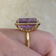 This beautiful gemstone ring centers an emerald cut, 12.50 carat, lively natural amethyst. Surrounding the gemstone is a halo of brilliant round diamonds that create a shared prong setting. The total diamond weight on this ring is approximately 0.42 carats. The mounting is handcrafted in 18k yellow gold and features a floral openwork under-gallery.
The measurements of this ring, including the halo, are approximately 19.04mm x 15.21mm.
This ring can be resized to any finger size at no additional cost.
If you have any questions regarding the Manorville ring, please feel free to contact us. Luxury Amethyst Ring With Emerald Cut Diamond, Luxury Emerald Cut Amethyst Ring With Diamond Setting, Luxury Emerald-cut Diamond Amethyst Ring, Luxury Amethyst Ring Emerald Cut, Luxury Emerald Cut Amethyst Ring, Elegant Purple Amethyst Baguette Cut Ring, Elegant Purple Baguette Cut Amethyst Ring, Luxury Emerald-cut Amethyst Ring For Formal Events, Luxury Emerald Cut Amethyst Ring For Formal Occasions