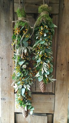 two wreaths with pine cones and berries hanging on a wooden door, covered in greenery