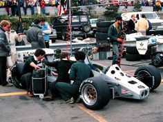 two men working on a race car in a parking lot with other people standing around