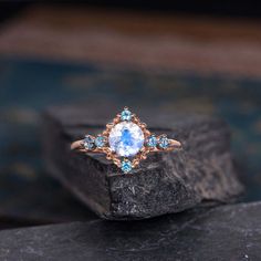 an engagement ring with blue topazte and diamonds on a rock in front of a dark background