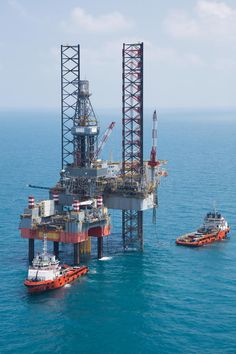 an oil rig in the middle of the ocean with tug boats around it on the water