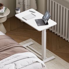 a laptop computer sitting on top of a white table next to a bed and radiator