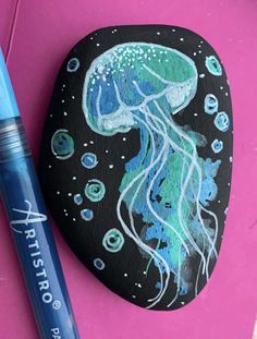 a rock with a drawing of a jellyfish on it next to a blue marker