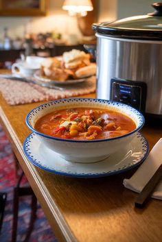 a bowl of soup sits on a table next to a crock pot