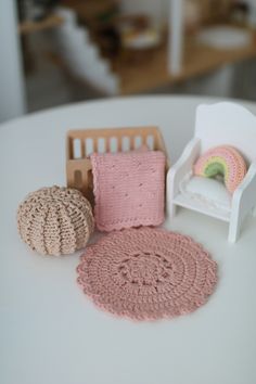 three crocheted items are sitting on a white table with a doll house in the background