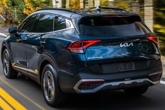 the rear end of a blue suv driving down a road with trees in the background