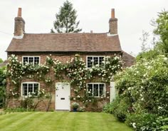 an old brick house with white flowers growing on it's windows and door, surrounded by greenery