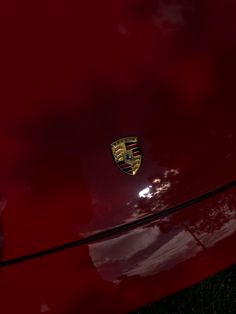 the front end of a red car with a gold emblem on it's hood