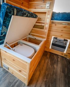 an open wooden box sitting on top of a hard wood floor next to a bed