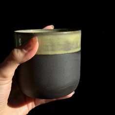 a hand holding a black and green cup in it's right hand, against a dark background