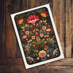 a card with an image of flowers and leaves painted on the front, sitting on a wooden surface