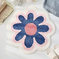 a blue and pink flower rug next to slippers on a white table with other items