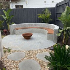 a stone bench sitting in the middle of a garden next to a tree and fence