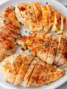 sliced chicken on a white plate with parsley and seasoning sprinkled around it