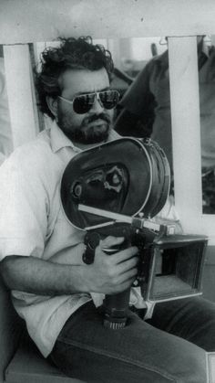 black and white photograph of a man sitting on a chair holding a camera in his hand