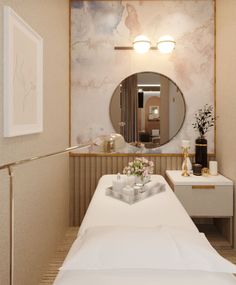 a white bed sitting under a mirror next to a table with flowers on top of it