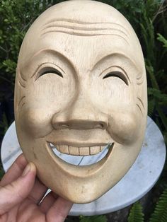 a person holding up a wooden mask with a smile on it