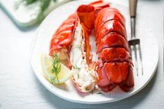 there is a lobster on the plate with lemon wedges and a fork next to it