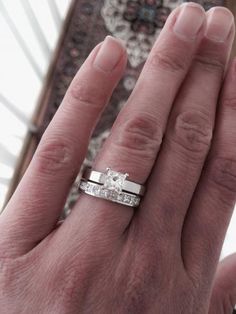 a person's hand with a wedding ring on top of their finger and the other hand holding an engagement ring