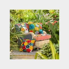 a chair with colorful pillows in the middle of some plants