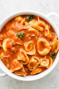 a white bowl filled with tortellini shells covered in tomato sauce and broccoli