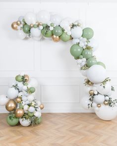 the balloon arch is decorated with white and green balloons, greenery and gold accents