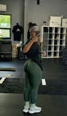 a woman taking a selfie in a gym with her cell phone and wearing tight green leggings