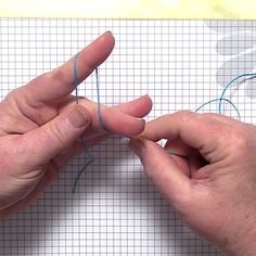 two hands are working with yarn on a piece of paper that is graphed out