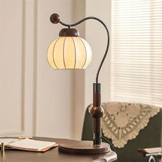 a desk lamp sitting on top of a wooden table next to a book and pen