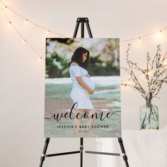 an easel with a welcome sign on it next to a vase and string lights