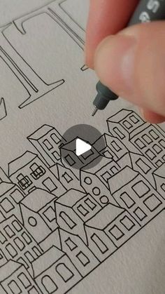 a person is holding a pen and drawing on paper with buildings in the background,