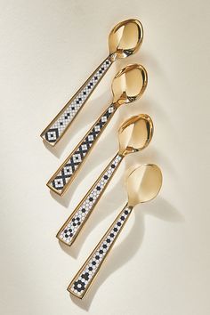 four gold spoons with black and white designs are lined up against a white background