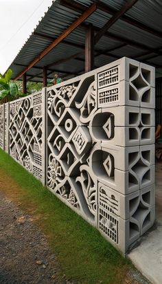 a cement wall with decorative carvings on it in front of a covered area and green grass