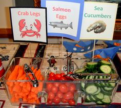 a table topped with lots of different types of vegetables and signs that read crab legs, salmon eggs, and cucumbers