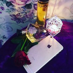 a bottle of perfume next to a rose and an ipad on a purple tablecloth