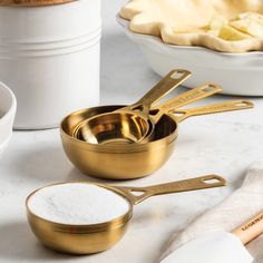 gold measuring cups and spoons are sitting on a marble countertop next to baking utensils