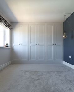 an empty room with blue walls and white cupboards on the far wall is a window