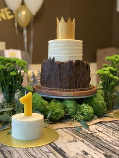 a cake on a table with greenery around it and balloons in the back ground