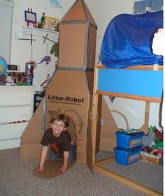 a young boy is playing in a cardboard rocket ship