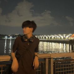 a young man standing on a bridge next to the water at night with buildings in the background